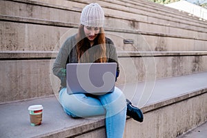 Portrait of freelancer woman using laptop while sitting on stairs in city street. Blogger concept.