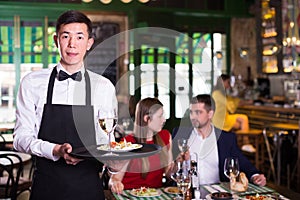 Portrait of frendly male waiter who is standing with tray