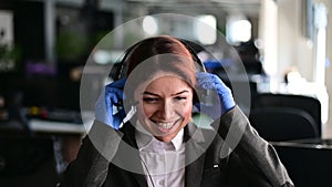 Portrait of friendly call center operator woman in gloves put on headset in office. A smiling female hotline employee in