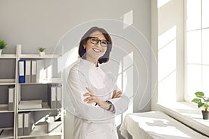 Portrait of a friendly female doctor standing in hospital with arms folded and looking at camera.