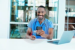 Portrait of a friendly male doctor or nurse wearing blue scrubs uniform and stethoscope sitting at desk