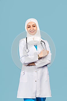 Portrait of a friendly, Muslim doctor or nurse woman in hijab with a stethoscope in a white coat. on a blue background