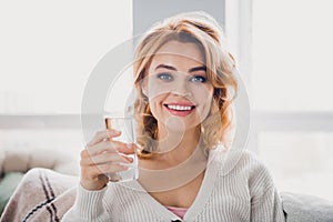 Portrait of friendly positive girl beaming smile sitting sofa hold glass fresh water bright house inside