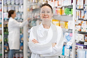 Portrait of friendly smiling female pharmacist in interior of pharmacy or store selling healing cosmetics