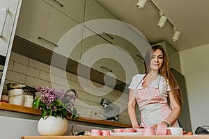 Portrait of friendly smiling female professional confectioner topping a cupcake with cream using a pastry bag. Looking