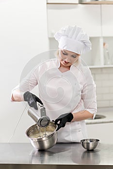 Portrait of friendly smiling female professional confectioner topping a cupcake with cream using a pastry bag