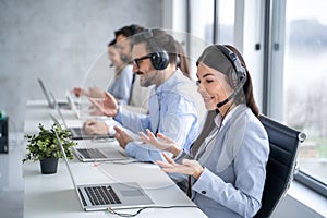 Portrait of friendly young female call center operator in headphones working with her colleagues at customer support service