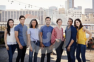 Portrait Of Friends Gathered On Rooftop Terrace For Party With City Skyline In Background