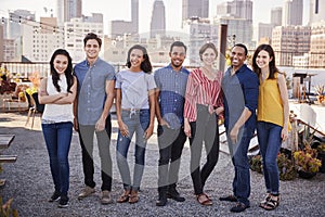 Portrait Of Friends Gathered On Rooftop Terrace For Party With City Skyline In Background