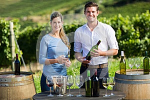 Portrait of friends holding wineglass and bottle by table against vineyard