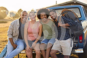 Portrait Of Friends Sitting On Tailgate Of Pick Up Truck On Road Trip To Cabin In Countryside