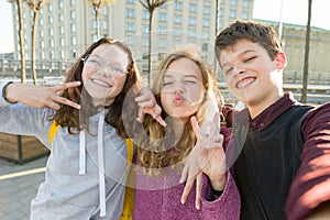 Portrait of friends teen boy and two girls smiling, making funny faces, showing victory sign in the street