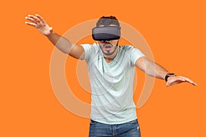 Portrait of frightened gamer, brunette man stretching hands forward, trying to grab something while playing virtual reality game