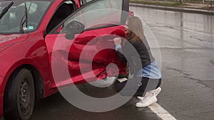 Portrait of a frightened girl near her broken car after a accident on a wet road