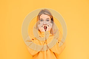 Portrait of a frightened girl on a yellow background looks shocked at the camera and bites her fingers. Isolated. Girl with light