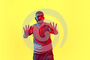 Portrait of frightened, scared, shocked young man, student in casual outfit isolated on yellow background in red neon