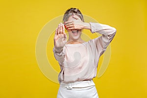 Portrait of frightened young woman with fair hair in casual beige blouse, isolated on yellow background