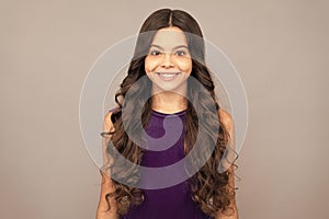 portrait of frizz child in purple dress. kid with curly hair. teen beauty hairstyle.