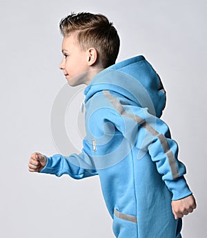 Portrait of frolic, active kid boy in blue jumpsuit with hood and pockets with reflective stripes running. Side view