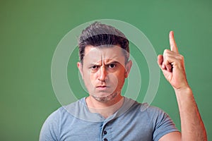 Portrait of frowing young man in casual clothes pointing fingers up. People, emotions, lifestyle concept photo