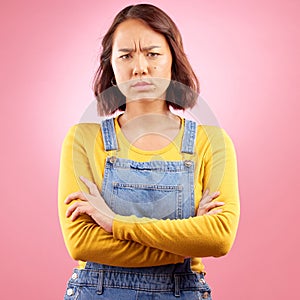 Portrait, frown and angry asian woman with arms crossed in studio and defensive body language on pink background. Wtf