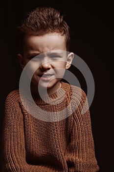 Portrait of frowning serious angry stylish white Caucasian child boy kid preschooler on a chair