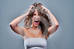 Portrait of a frustrated angry woman screaming out loud and pulling her hair out  on the gray background