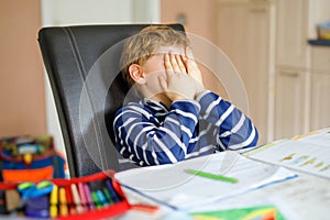 Portrait of frustrated crying sad school kid boy at home making homework. Little child writing with colorful pencils