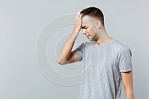 Portrait of frustrated crying young man in casual clothes keeping eyes closed putting hand on head isolated on grey