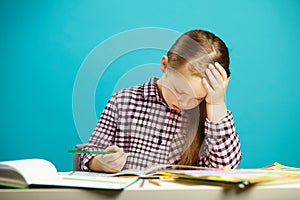 Portrait of frustrated girl at desk with textbooks, expresses fatigue and disappointment, put hand to head, puzzle over