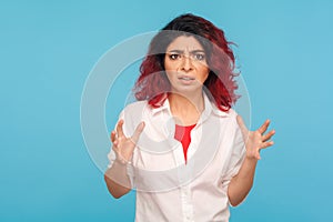 Portrait of frustrated hipster woman with fancy red hair in shirt standing angry with raised hands, ready to quarrel