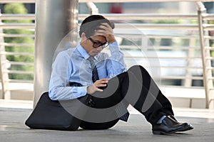 Portrait of frustrated stressed young Asian man sitting on the floor of sidewalk office and feeling tired with job