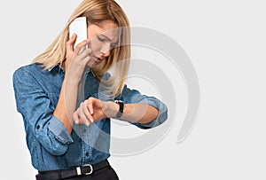 Portrait of frustrated young blonde woman talking on mobile phone, looking at the watch, because her colleague is late