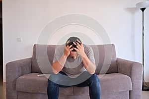 Portrait of a frustrated young man sitting on a sofa with his hands on his head