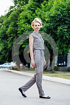 Portrait full length of attractive 40 years old woman walking outdoors among green trees in alley. Middle aged smiling