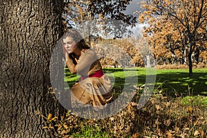 Portrait full shot elegant young woman crouch in the ground. Tree. Thoughtful. In love. Autumn