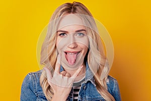 Portrait of funky positive rock fan girl showing horns sign protrude tongue on yellow background photo
