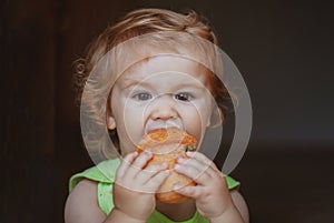 Portrait of funny baby with bread in her hands eating. Cute toddler child eating sandwich, self feeding concept.