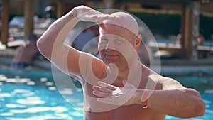 Portrait, funny bald middle-aged man, with a naked torso, something fun sings, dances, by the pool on vacation, in