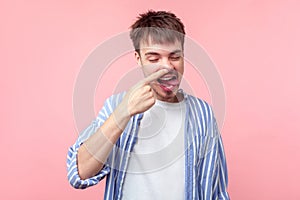 Portrait of funny brown-haired man with small beard and mustache picking his nose. indoor studio shot isolated on pink background