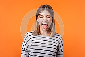 Portrait of funny carefree young woman with brown hair in long sleeve striped shirt. indoor studio shot isolated on orange
