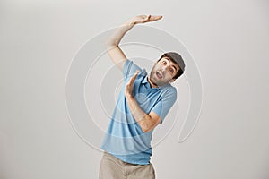 Portrait of funny caucasian guy raising hands up as if defending from something falling from sky or carrying heavy