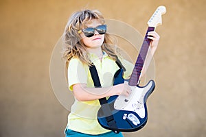 Portrait of a funny child with glasses practicing a song during a guitar lesson on street. Music concept, kids music