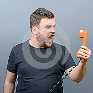 Portrait of funny chubby man shouting on phone against gray background