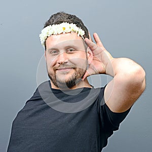 Portrait of funny chubby man wearing flower wreath on head and behaving feminine against gray background photo