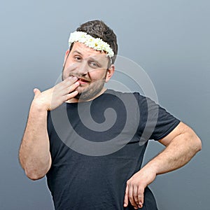 Portrait of funny chubby man wearing flower wreath on head and behaving feminine against gray background photo