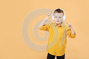 portrait of funny clever school boy with headphones in yellow shirt. Yellow studio background. Education. Looking and