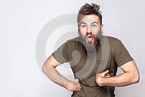 Portrait of funny crazy bearded man with tongue out and dark green t shirt against light gray background.