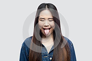Portrait of funny crazy beautiful brunette asian young woman in casual blue denim jacket with makeup standing with closed eyes and