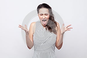 Portrait of funny crazy beautiful young brunette woman with makeup and striped dress standing with crossed hands and tongue out